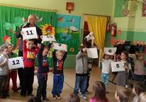 Dzieci unoszą w górę ręce trzymając kartki, na których zostały wydrukowane cyfry.